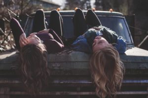 two women laying on old car laughing