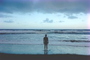 man standing with feet on the shore looking out at ocean 