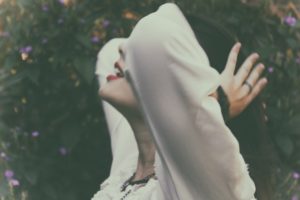 woman with head tilted up holding her hair next to trees