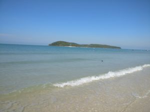 beach with blue sky, blue water, and a green island in the distance 