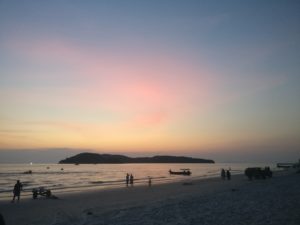 pink streaks in a blue sky with orange along the horizon at sunset on a beach