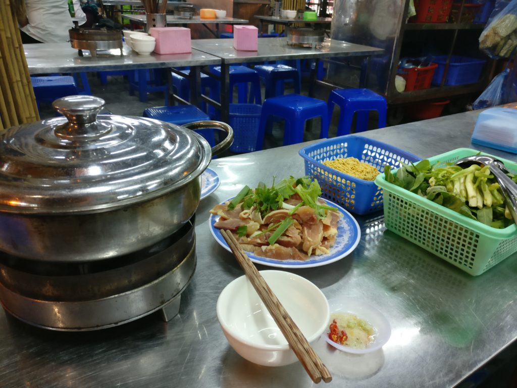 a hot pot with a bowl of raw meat and basket of vegetables ready to be cooked at the dong xuan night market