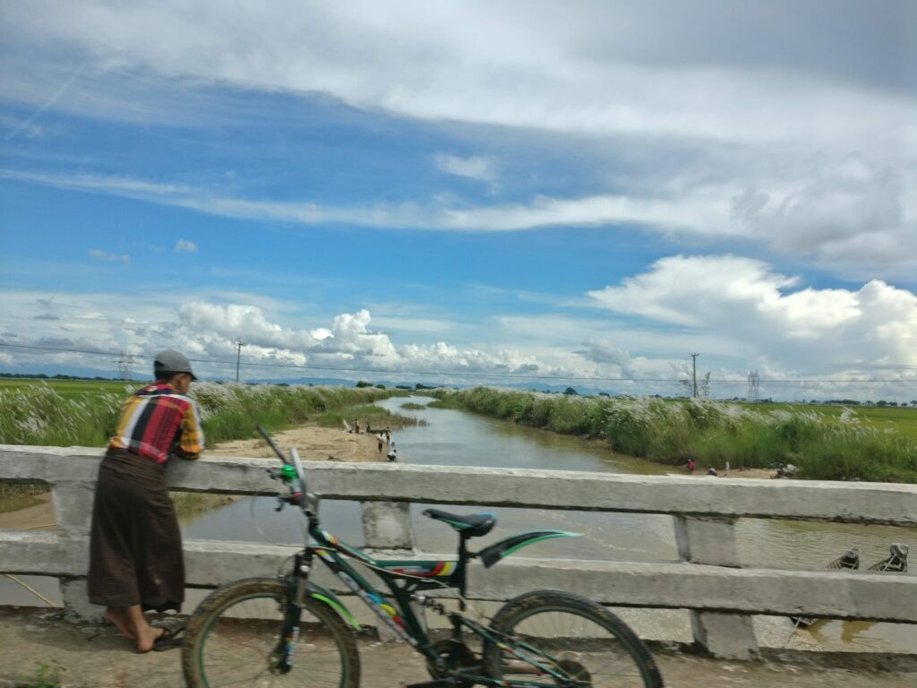 Man looking over a bridge next to his bike in Myanmar