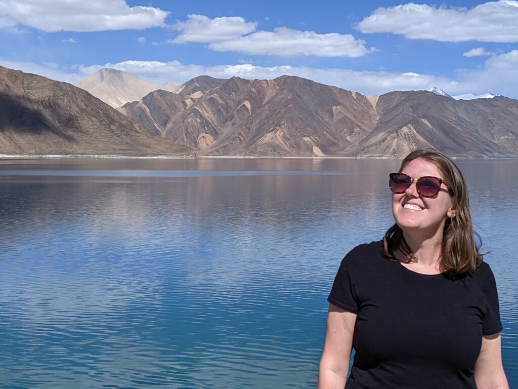 Woman smiling in front of a beautiful lake with mountains looking excited to be starting a new chapter
