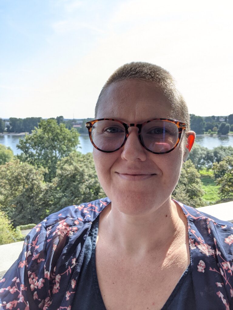 Kayla Dhankhar standing on a balcony with a beautiful river view behind her